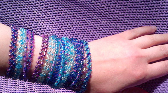 forearm almost covered with a series of bead bracelets in purple, turquoise and silver colours